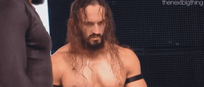 A Shirtless Wrestler With Long Hair And A Beard Is Standing In Front Of A Large Screen . GIF