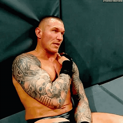 A Shirtless Wrestler With Tattoos On His Arms Is Sitting On The Floor GIF