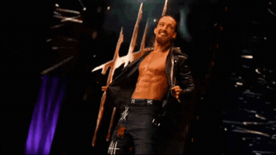 A Shirtless Wrestler With The Letter X On His Shorts Is Standing On A Stage GIF