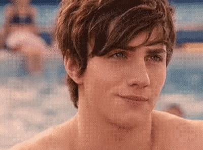 A Shirtless Young Man Is Standing In Front Of A Swimming Pool Looking At The Camera . GIF