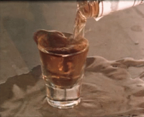 A Shot Glass Is Being Poured From A Bottle On A Table GIF