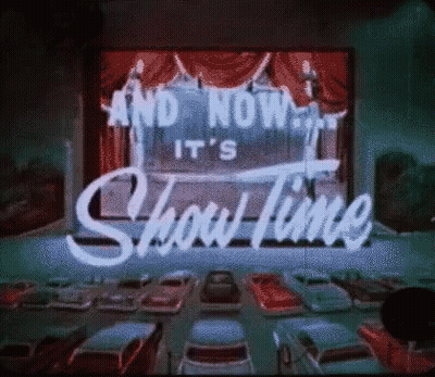 A Sign That Says " And Now It 'S Show Time " In Front Of A Drive In Theater GIF