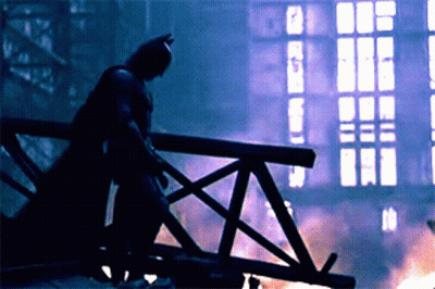 A Silhouette Of A Man In A Batman Costume Stands On A Bridge GIF