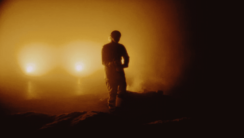 A Silhouette Of A Man Standing In Front Of A Glowing Light GIF