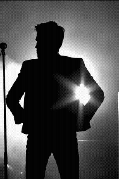 A Silhouette Of A Man Standing In Front Of A Microphone With His Hands On His Hips GIF