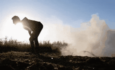 A Silhouette Of A Person Standing In A Field With Smoke Coming Out Of The Ground GIF