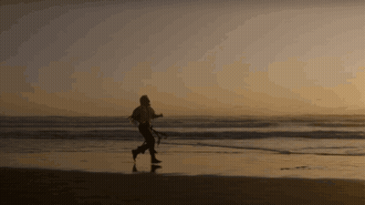 A Silhouette Of A Person Walking On The Beach At Sunset GIF