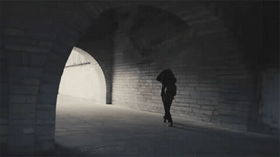 A Silhouette Of A Person Walking Through A Tunnel With Arches GIF