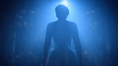 A Silhouette Of A Woman In A Blue Dress Is Standing In A Dark Room . GIF
