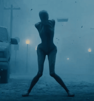A Silhouette Of A Woman Standing In A Foggy Street GIF