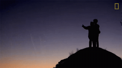 A Silhouette Of Two People Standing On Top Of A Hill GIF