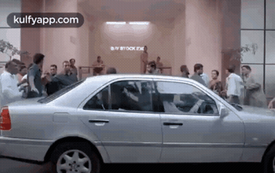 A Silver Car Is Parked In Front Of A Building With A Crowd Of People Standing Around It . GIF