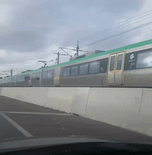 A Silver Train With A Green Top Is Going Down A Road GIF