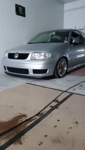 A Silver Volkswagen Is Parked In A Garage With A Monster Poster On The Wall Behind It GIF