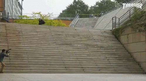 A Skateboarder Is Doing A Trick On A Set Of Stairs With A Thrasher Logo Behind Him GIF