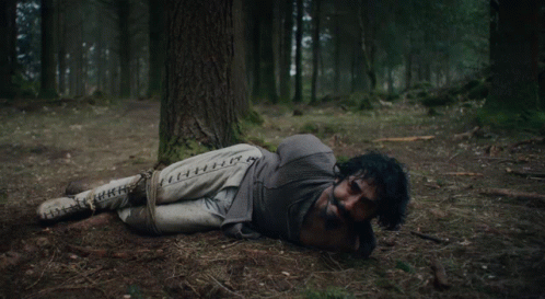 A Skeleton Laying Under A Tree In A Forest GIF