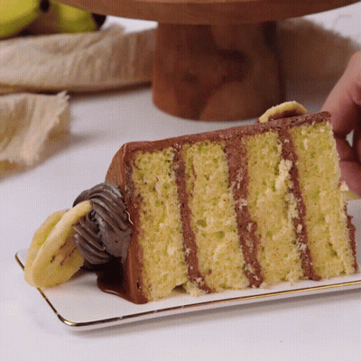A Slice Of Banana Cake With Chocolate Frosting On A Plate GIF