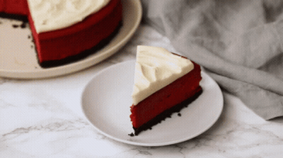 A Slice Of Red Velvet Cheesecake With White Frosting On A Plate GIF