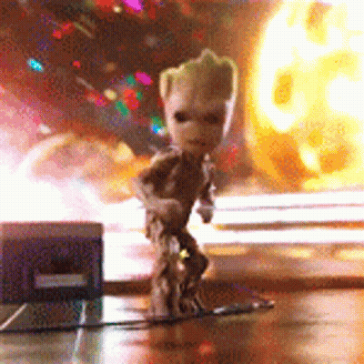 A Small Figurine Of Groot Is Standing On A Table In Front Of A Fireball . GIF