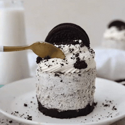A Small Oreo Cheesecake On A White Plate With A Gold Spoon GIF