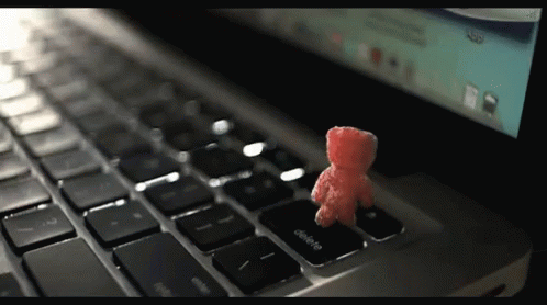 A Small Red Teddy Bear Sits On The Delete Key On A Laptop Keyboard GIF