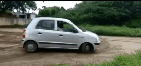 A Small Silver Car Is Driving On A Dirt Road . GIF