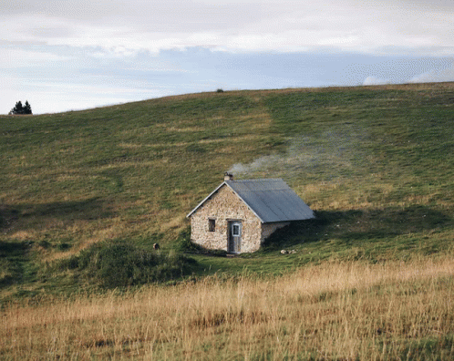 A Small Stone House Sits On Top Of A Grassy Hillside GIF