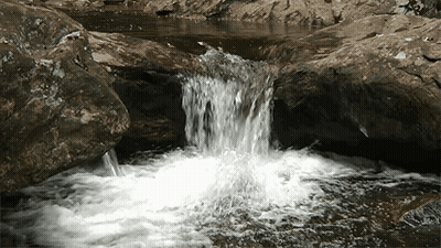 A Small Waterfall Is Surrounded By Rocks And A Small Pool Of Water GIF