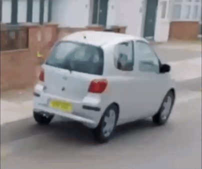 A Small White Car Is Driving Down A Street With A Yellow License Plate That Says ' A ' On It GIF