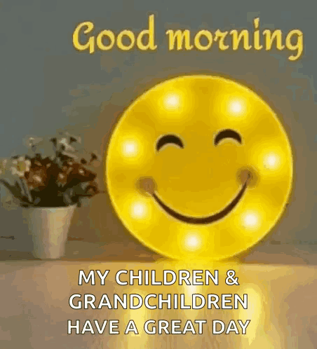 A Smiley Face Is Sitting On A Table Next To A Vase Of Flowers And A Good Morning Message . GIF