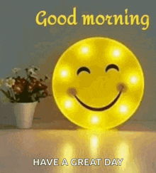 A Smiley Face Is Sitting On A Table Next To A Vase Of Flowers And Says `` Good Morning Have A Great Day '' . GIF
