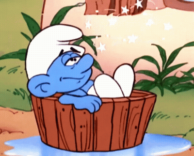A Smurf Is Sitting In A Wooden Tub With His Feet In The Water GIF