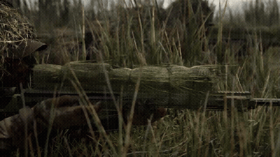 A Sniper Is Standing In The Grass With A Rifle In His Hand GIF