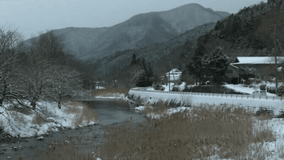 a snowy river with mountains in the background and a house in the foreground