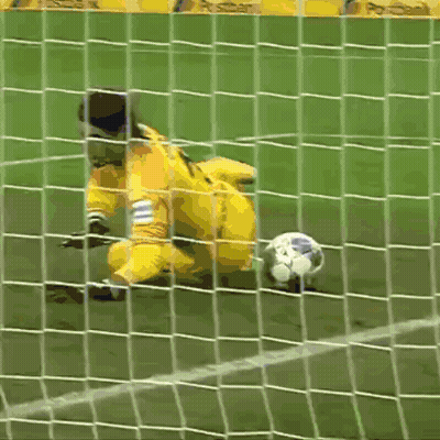 A Soccer Goalie Dives To Catch A Ball With A Postbank Banner In The Background GIF