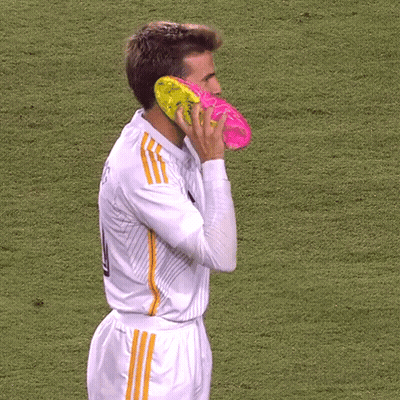 A Soccer Player Has A Pair Of Pink And Yellow Soccer Cleats On His Face GIF