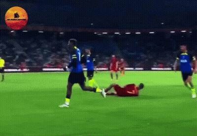 A Soccer Player In A Blue Jersey Is Running Towards A Player In A Yellow Jersey Who Is Laying On The Ground GIF