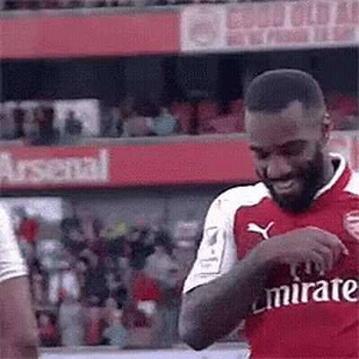 A Soccer Player In A Red Emirates Jersey Is Standing On A Field . GIF