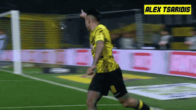 A Soccer Player In A Yellow Jersey Is Running On The Field With Alex Tsaridis In The Background GIF