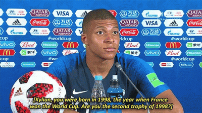 A Soccer Player Is Giving A Press Conference With A Bottle Of Water And A Soccer Ball Behind Him GIF