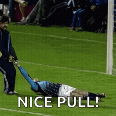 A Soccer Player Is Laying On The Ground While A Referee Pulls Him To The Goal . GIF