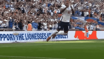 A Soccer Player Jumps In The Air In Front Of A Sign That Says Support The Lioness GIF