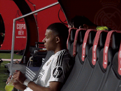 A Soccer Player Sits In A Dugout With A Sign That Says Copa Rey In The Background GIF