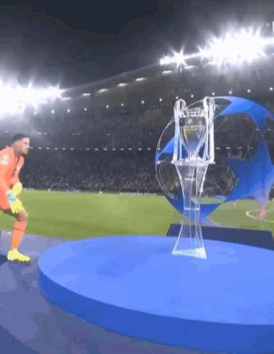 A Soccer Player Stands In Front Of A Trophy That Says Manchester City GIF