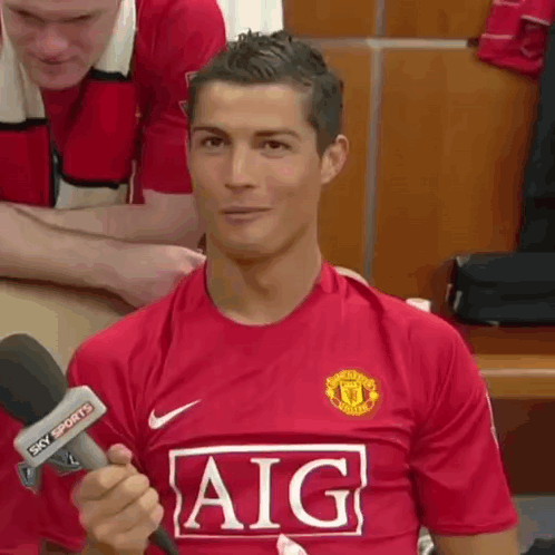 A Soccer Player Wearing A Red Aig Jersey Is Holding A Microphone . GIF