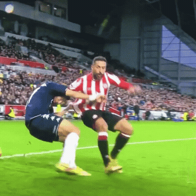 A Soccer Player Wearing A Red And White Striped Shirt Is Being Tackled By Another Player GIF