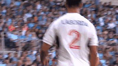 A Soccer Player Wearing A White Jersey With The Number 2 On The Back Is Walking In Front Of A Crowd . GIF
