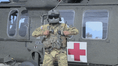 A Soldier Is Standing In Front Of A Helicopter With A Red Cross On The Door GIF