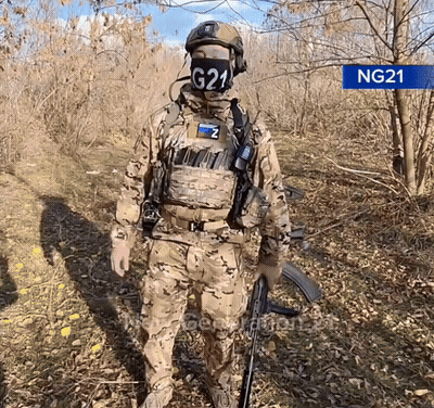 A Soldier Wearing A Mask With G21 On It Stands In The Woods GIF