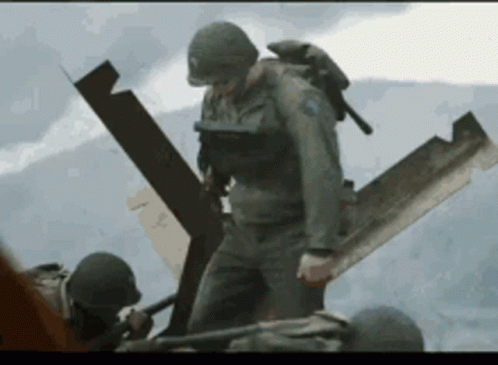 A Soldier With A Blue Patch On His Chest Is Standing Next To Another Soldier Holding A Shovel GIF